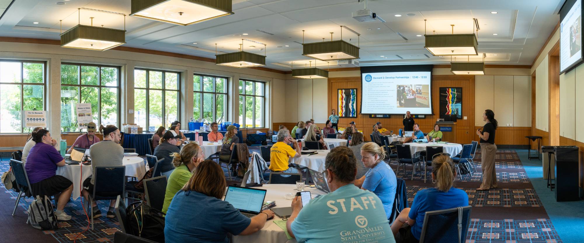 learning adults sitting down in a conference room space, adults around tables listening to presenter
